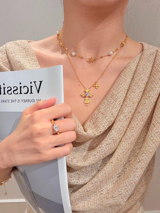 Overhead flatlay of gold gothic cross necklace with purple amethyst stone on white background.