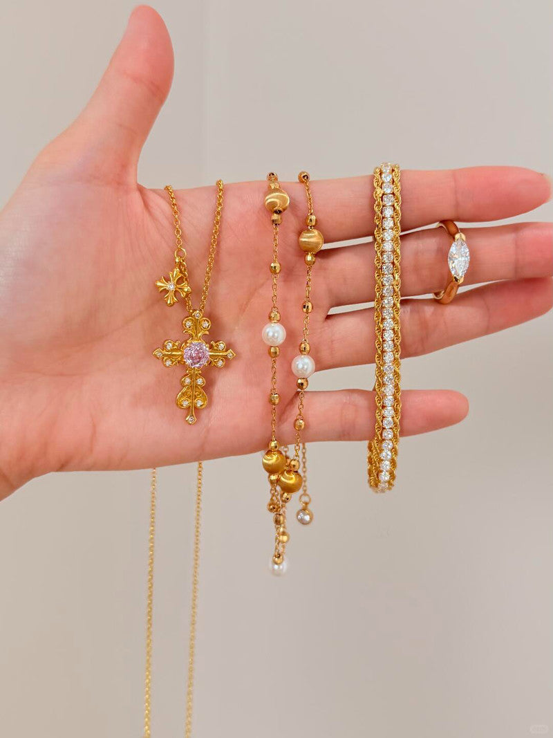 Hand holding various gold jewelry items including necklaces, bracelets, and rings on a neutral background