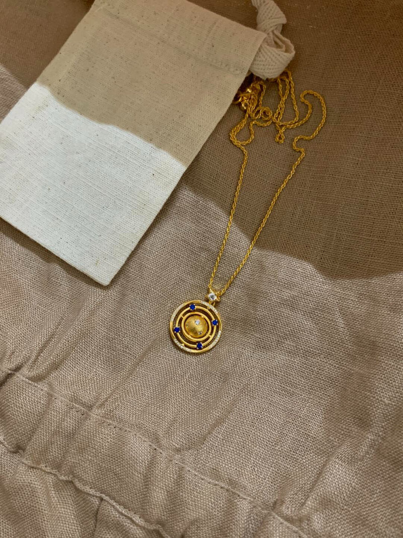 Gold necklace with a circular pendant on a textured brown surface
