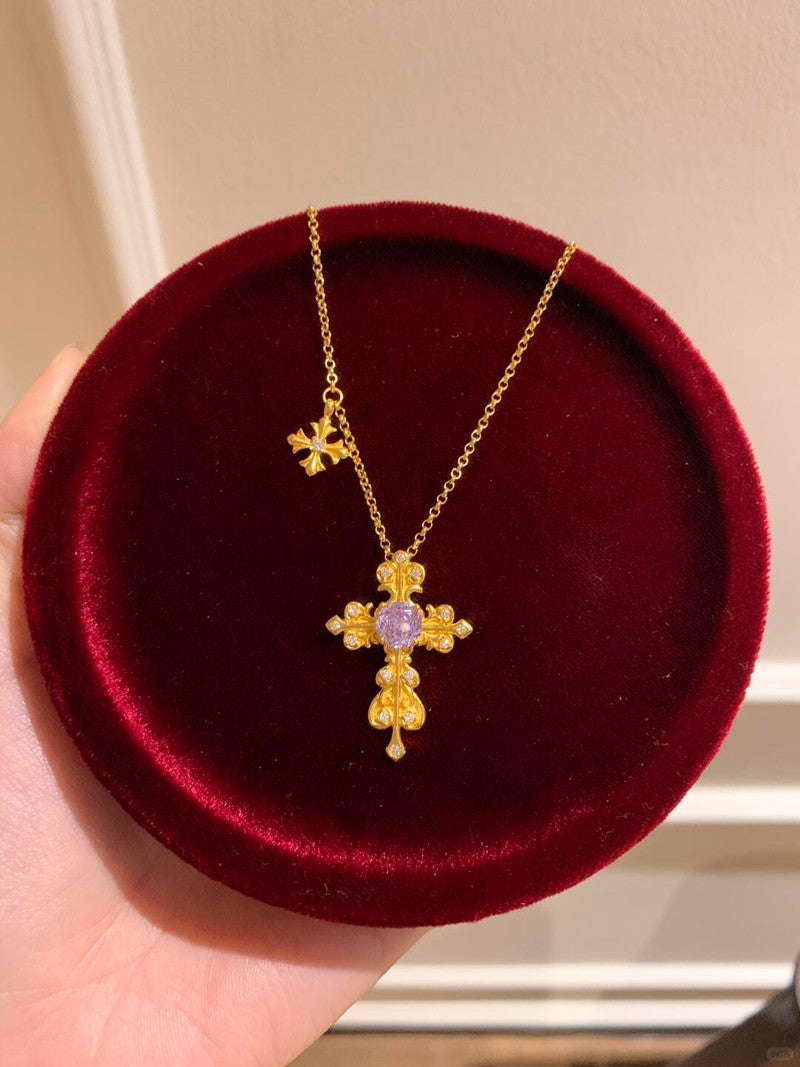 Gold cross necklace with a purple gemstone on a red velvet cushion.